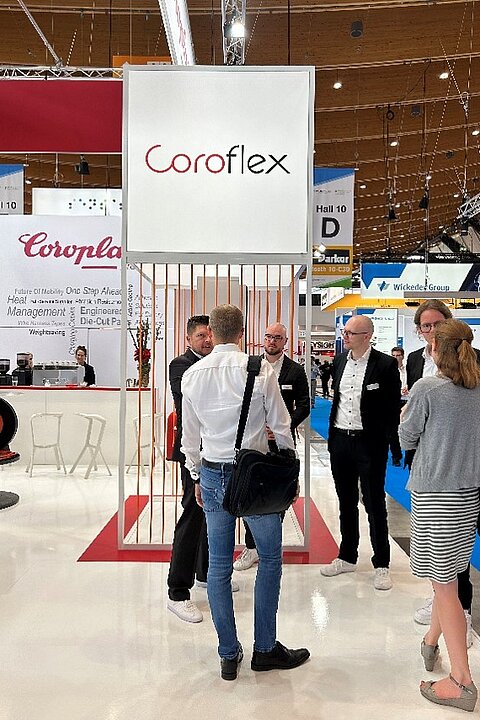 People gather and engage in conversation at the Coroflex exhibition area at the Battery Show 2024.