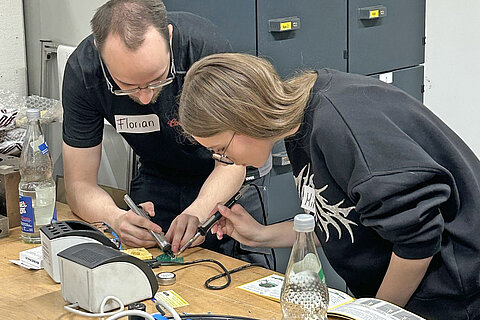 An apprentice shows a student how to solder a circuit board.