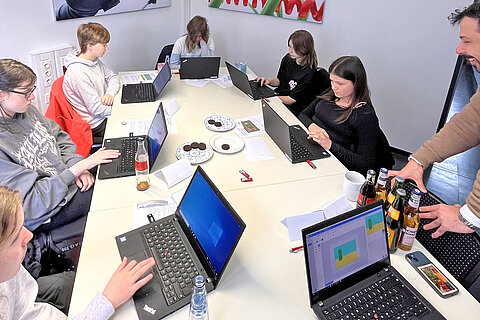 Sechs Mädchen zusammen mit dem Coroplast Group Auszubildenden Tim Potempa vor ihren Laptops.