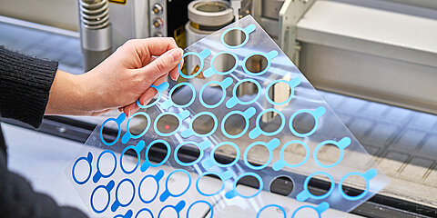 Employee presenting a customized die-cut part in front of a production machine