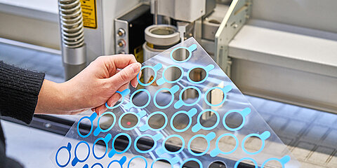 Employee presenting a customized die-cut part in front of a production machine