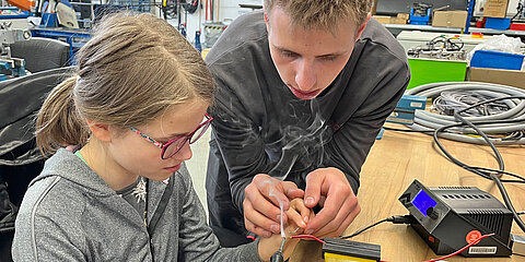 Apprentice explains the use of a soldering iron to a participant