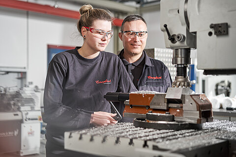 Angehende Industriemechanikerin und ihr Ausbilder an einer Maschine 